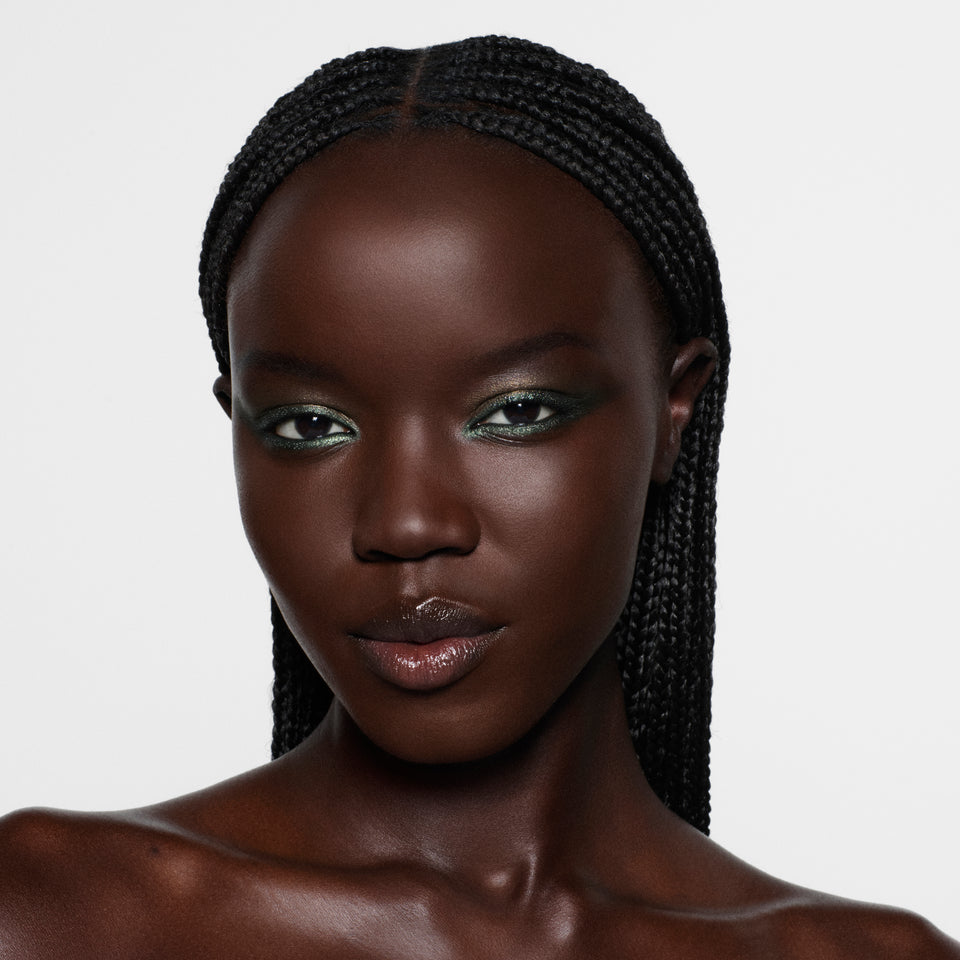 Deep-complexion model with long braids wearing a metallic olive green liner — Victoria Beckham Beauty Olive Eye Kit look.