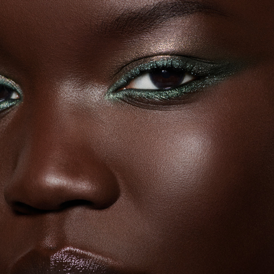 Close-up of a metallic olive green winged liner on a deep-complexion model — Victoria Beckham Beauty Olive Eye Kit look.