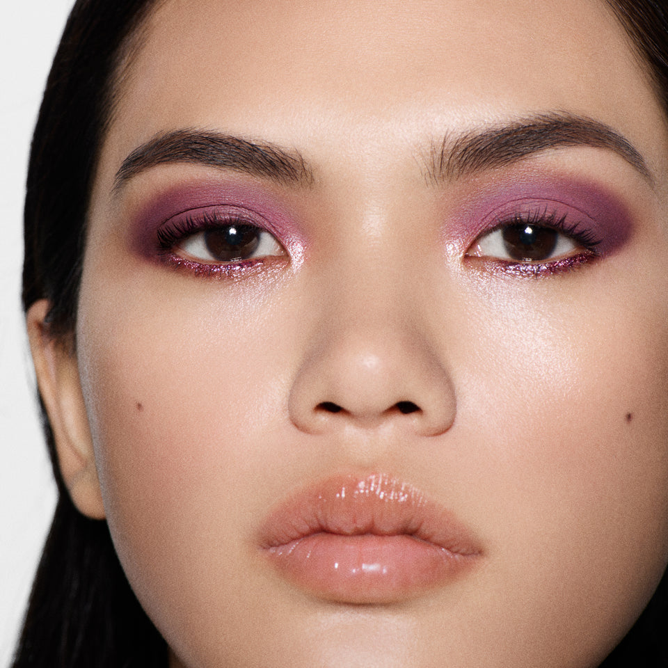 Close-up of an orchid violet shimmer eye and glossy nude lip on a light-tan model — Victoria Beckham Beauty Orchid Eye Kit look.