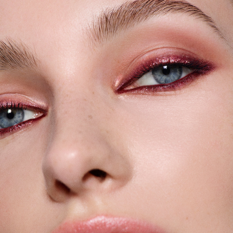 Close-up of blue eyes with rose-gold shimmer lids and burgundy liner — Victoria Beckham Beauty Bordeaux Eye Kit look.