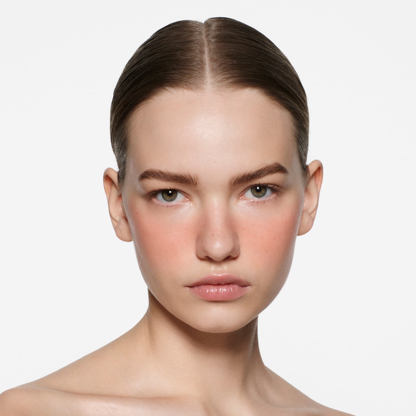 Fair-skinned model with slicked-back dark blonde hair and coral peach blush in Blush Stylus Fresco by Victoria Beckham Beauty.
