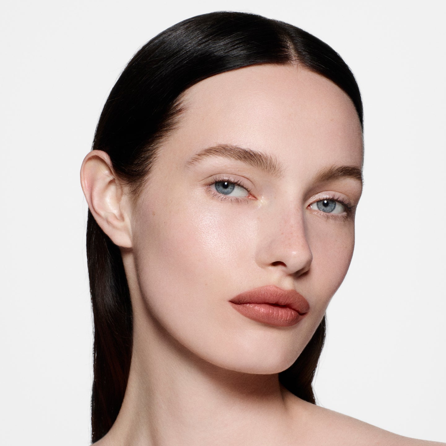 Fair-skinned model with sleek centre-parted dark hair in Lip Definer No. 1.5 — warm rosy-taupe by Victoria Beckham Beauty.