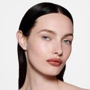 Fair-skinned model with sleek centre-parted dark hair in Lip Definer No. 1.5 — warm rosy-taupe by Victoria Beckham Beauty.