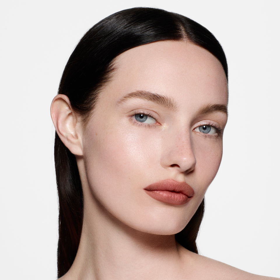 Fair-skinned model with sleek centre-parted dark hair in Lip Definer No. 1.5 — warm rosy-taupe by Victoria Beckham Beauty.