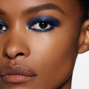 Close-up of a model's face showcasing a vibrant blue shimmery eyeshadow look with defined black winged eyeliner and neutral brown lipstick.