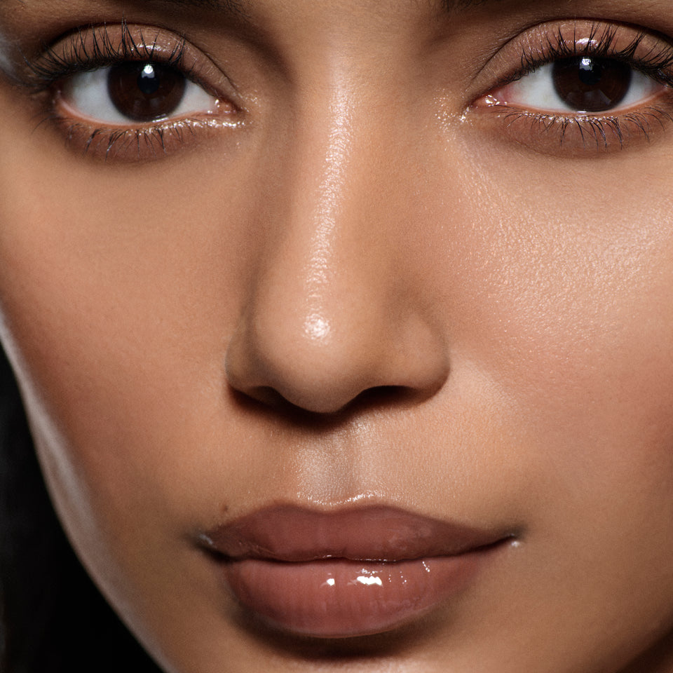 Close-up of tan lips glazed in Posh Gloss Poolside — Victoria Beckham Beauty's cocoa brown mirror-shine lip gloss.