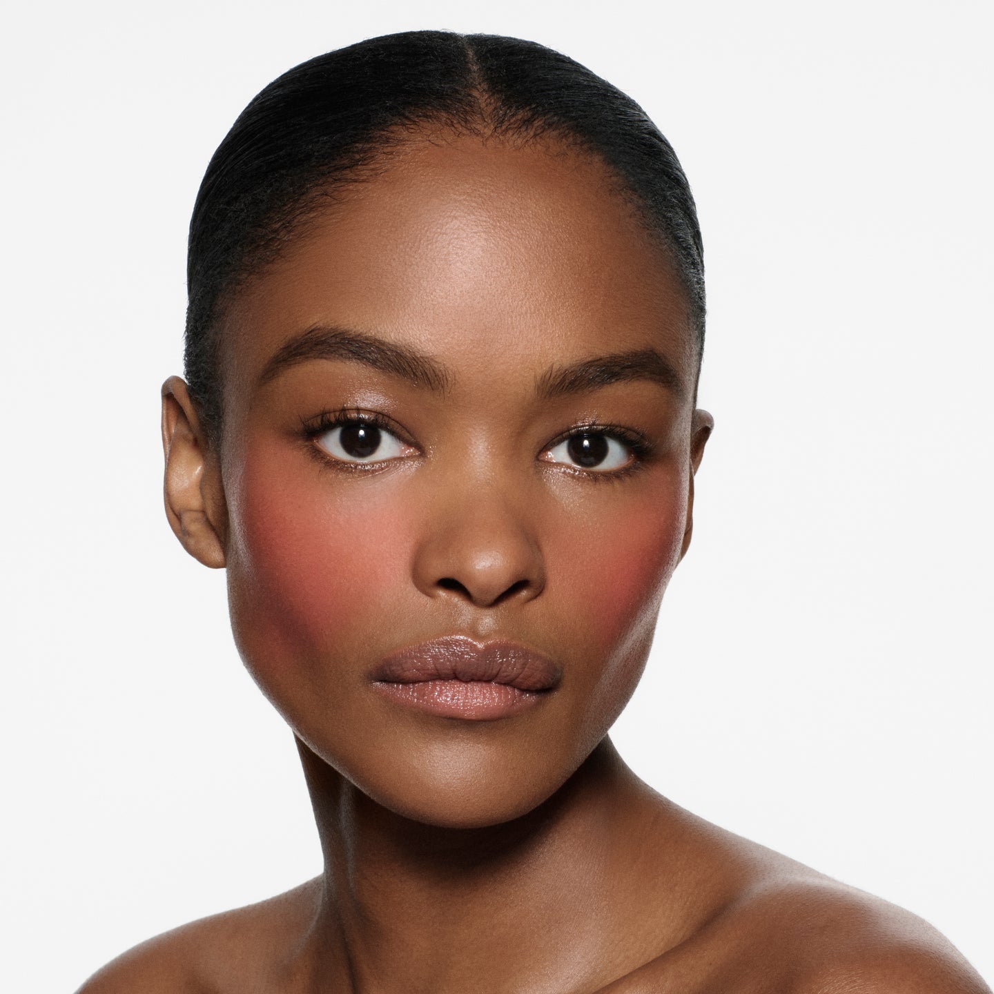 Medium-brown complexion model with slicked dark hair and warm rose flush in Blush Stylus Rossa by Victoria Beckham Beauty.