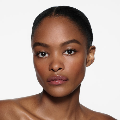 Deep-complexion model with slicked-back hair wearing Posh Gloss Fizz — mauve berry lip gloss by Victoria Beckham Beauty.