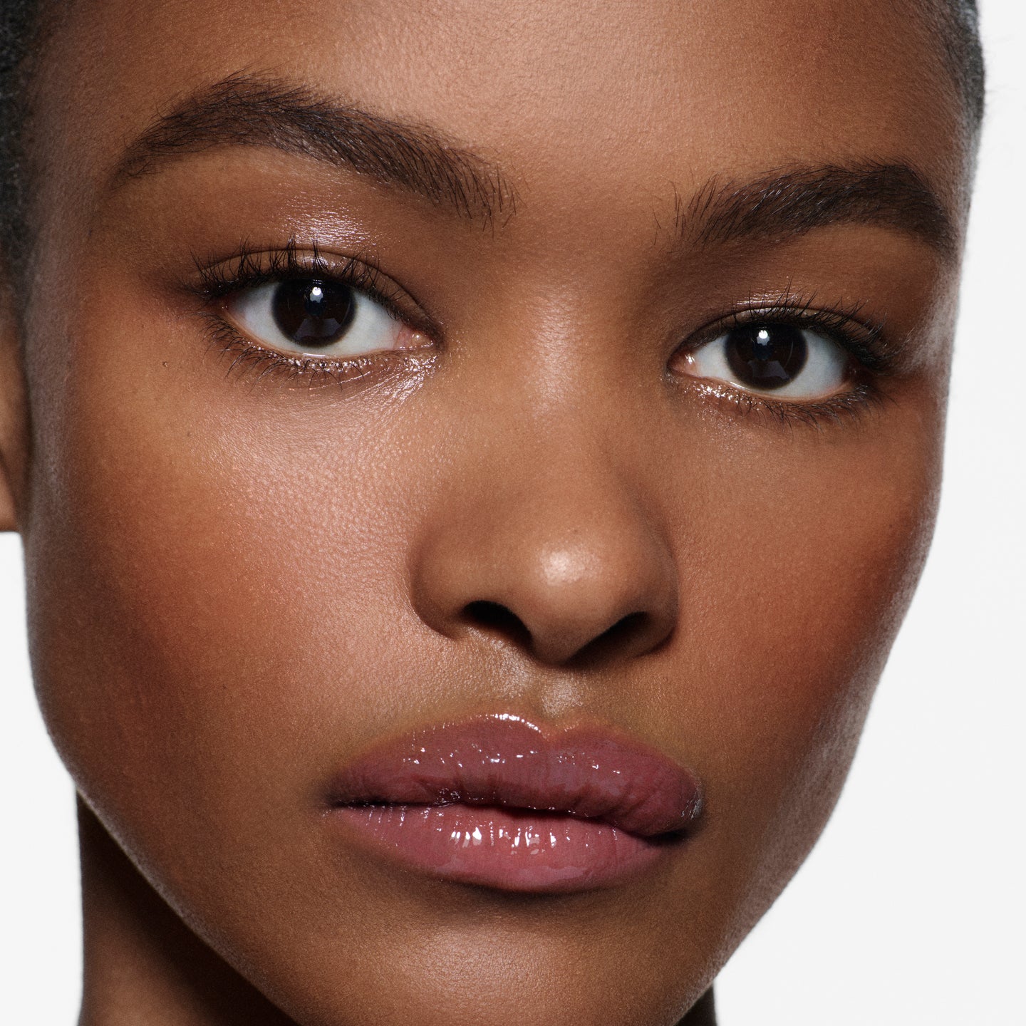 Close-up of lips on deep complexion in Posh Gloss Fizz — Victoria Beckham Beauty's mauve berry mirror-shine gloss.