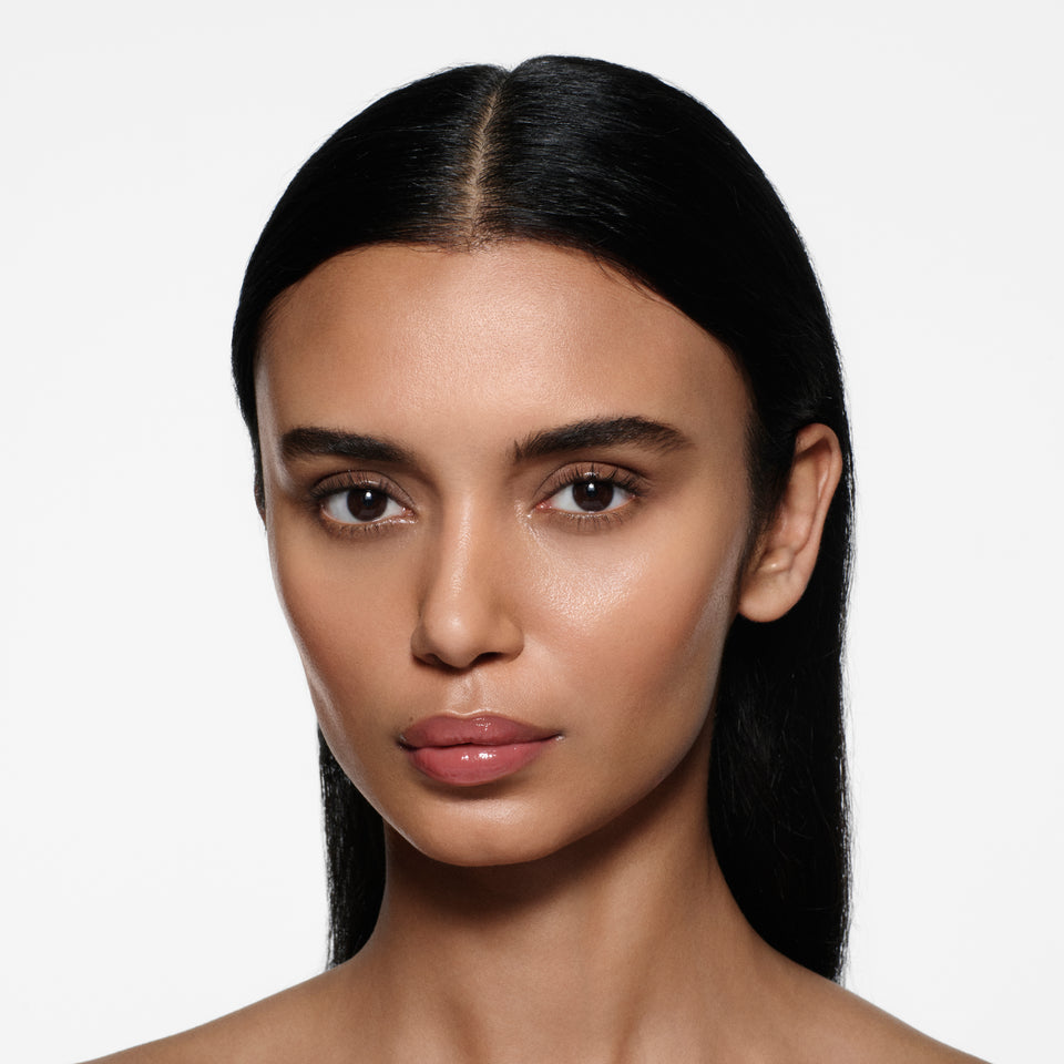 Olive-complexion model with long sleek dark hair wearing Posh Gloss Cabana — dusty rose pink by Victoria Beckham Beauty.