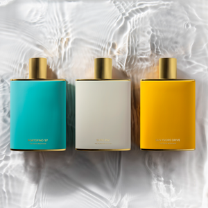 Three bottles of Fragrance lay down next to each other, against a watery background.
