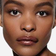 Close-up of glossy lips on brown complexion in Posh Gloss Aperitivo — Victoria Beckham Beauty's rosewood-plum mirror-shine gloss.