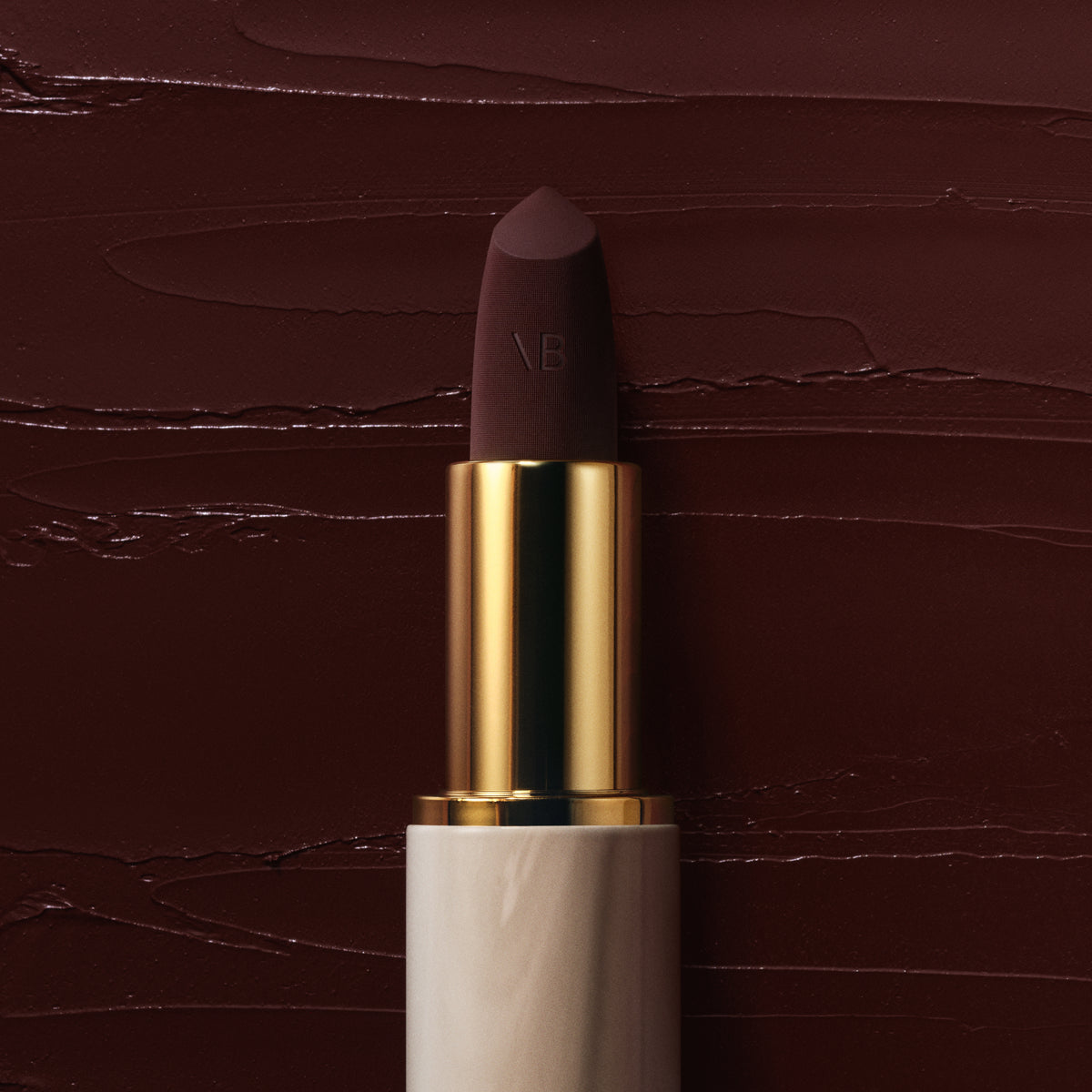 Rouge Victoria in Minuit, cream and gold case, on a swatch of the blackened plum shade — Victoria Beckham Beauty.