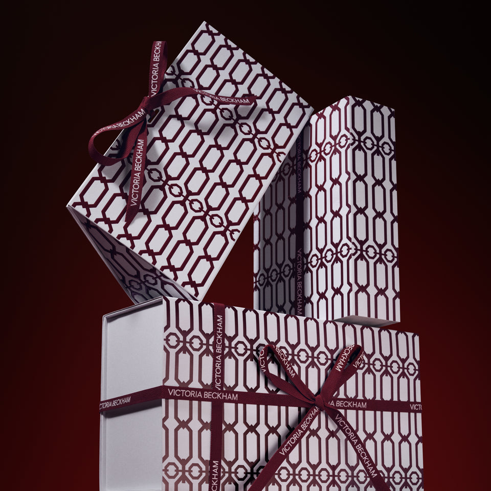 Stacked gift boxes in a burgundy trellis print, tied with branded ribbon bows — Victoria Beckham Beauty holiday gift packaging.