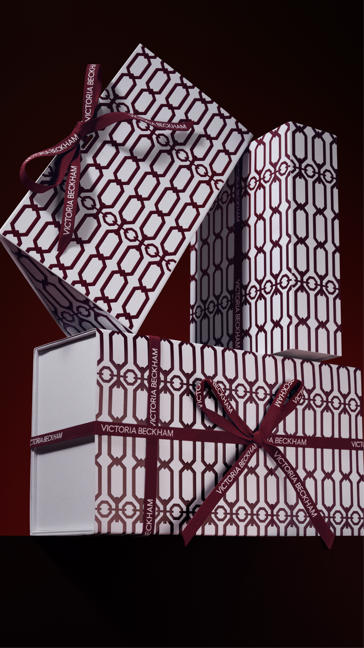 Stacked gift boxes in a burgundy trellis print, tied with branded ribbon bows — Victoria Beckham Beauty holiday gift packaging.