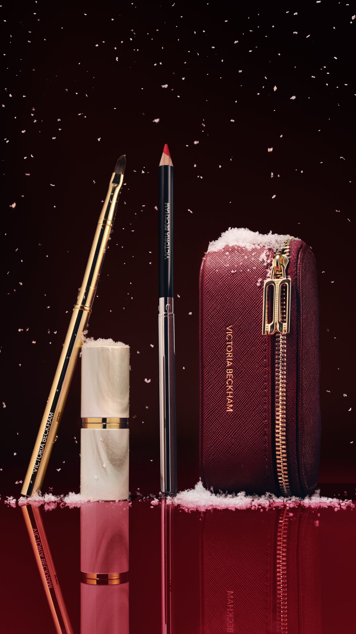 Gold lip brush, marble-cap lipstick, lip pencil and burgundy zip case in falling snow — Victoria Beckham Beauty holiday lip edit.