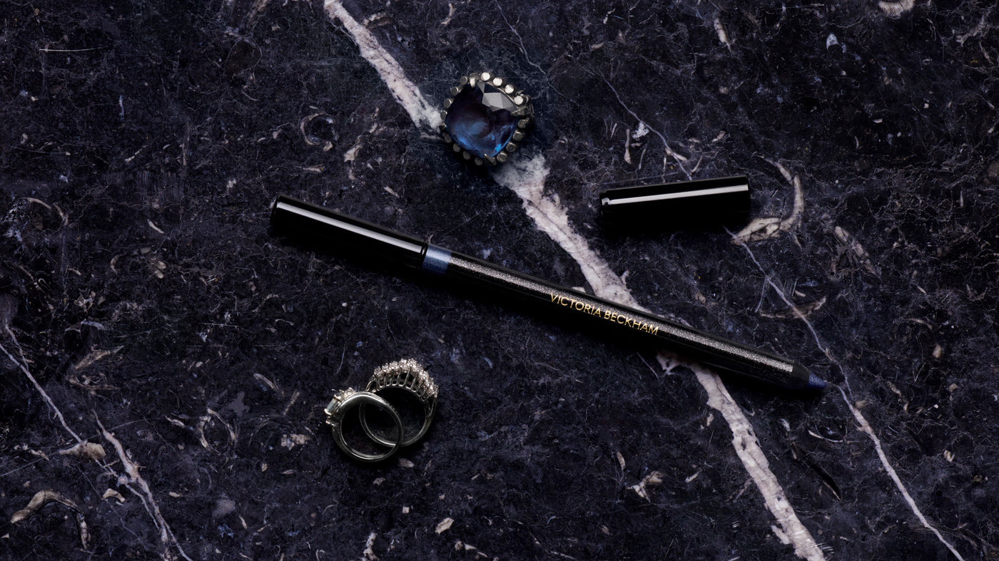 Navy Satin Kajal Liner on black marble with a sapphire ring and pavé bands — Navy Noir by Victoria Beckham Beauty.