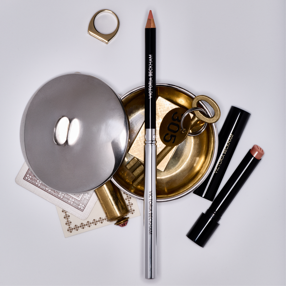Victoria Beckham Beauty Lip Definer and two Posh Lip bullets styled on a gold tray with a ring and playing cards.