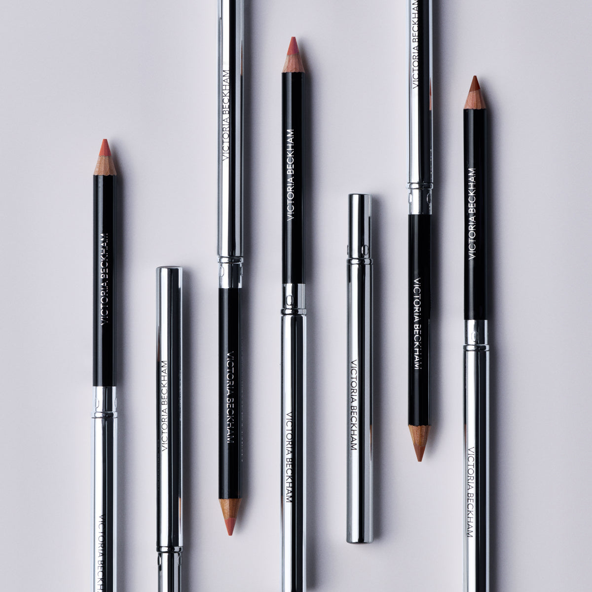 Seven Victoria Beckham Beauty Lip Definer pencils laid alternating, sharpened tips bared, full shade range on show.