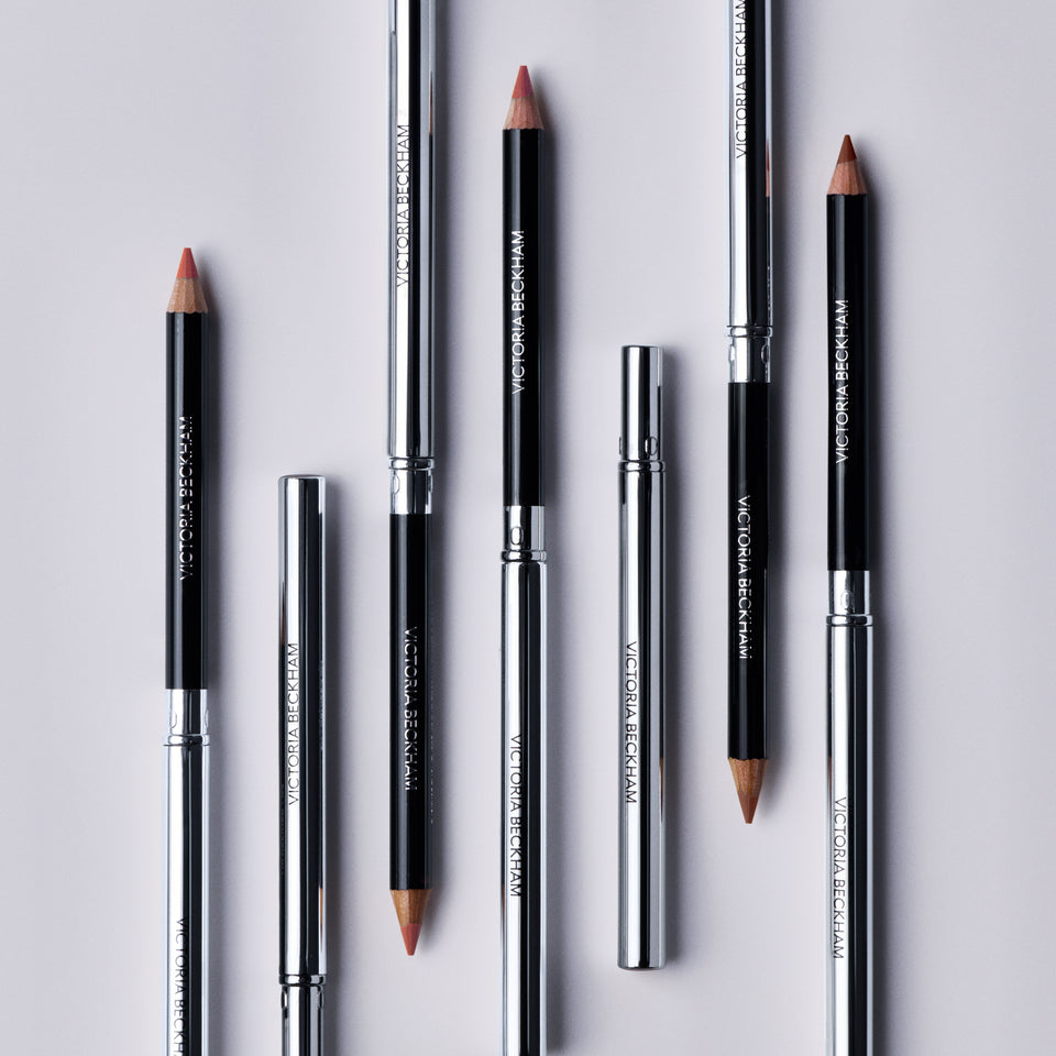 Seven Victoria Beckham Beauty Lip Definer pencils laid alternating, sharpened tips bared, full shade range on show.