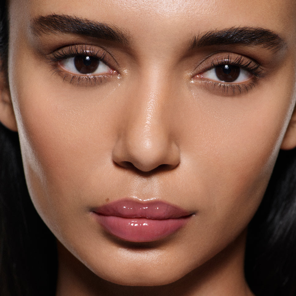 Close-up of tan lips glossed in Posh Gloss Fizz — Victoria Beckham Beauty's mauve berry high-shine lip gloss.