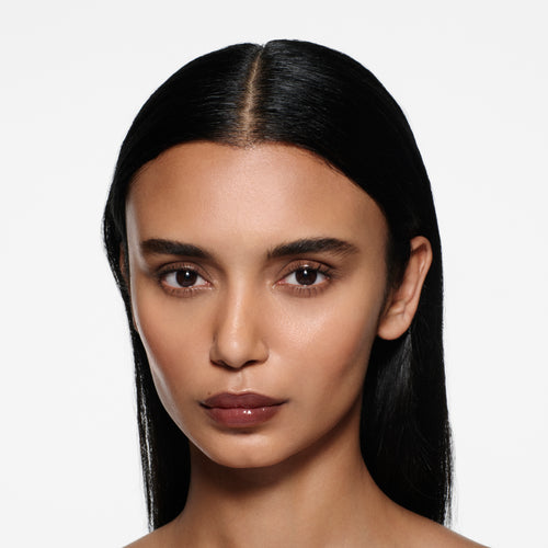 Tan-complexion model with long sleek dark hair wearing Posh Gloss TopDown — deep mahogany by Victoria Beckham Beauty.