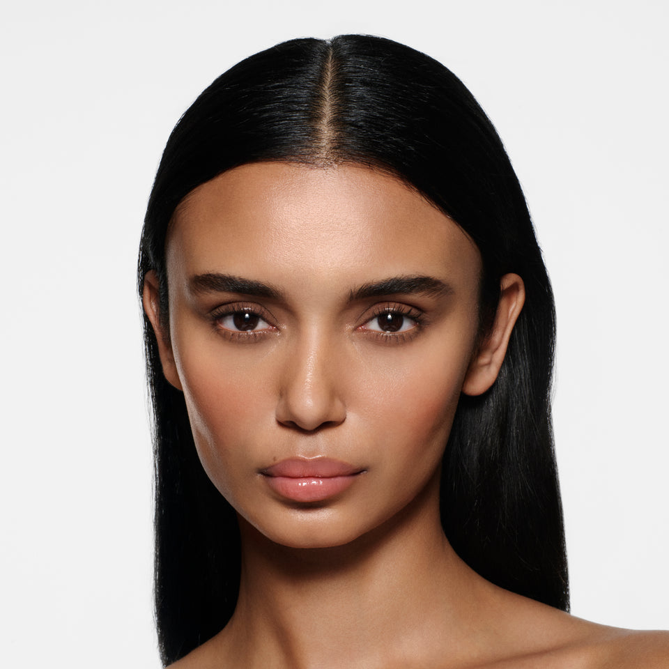Tan-complexion model with long sleek dark hair wearing Posh Gloss Picante — vivid coral salmon by Victoria Beckham Beauty.