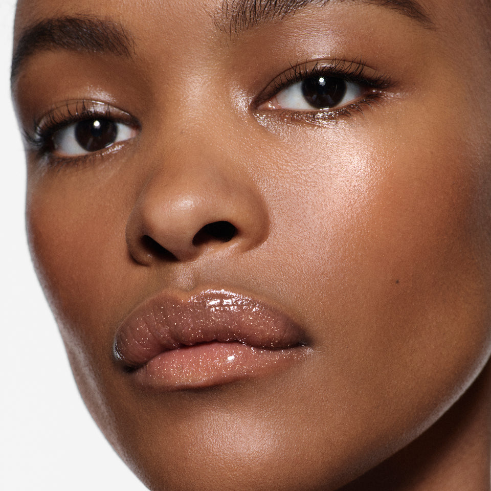 Close-up of brown lips glazed in Posh Gloss Martini — Victoria Beckham Beauty's champagne gold shimmer lip gloss.
