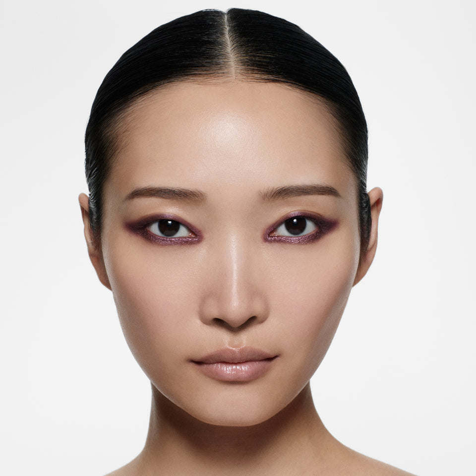 Close-up of a person wearing purple shimmer eyeliner with a neutral expression on a plain background