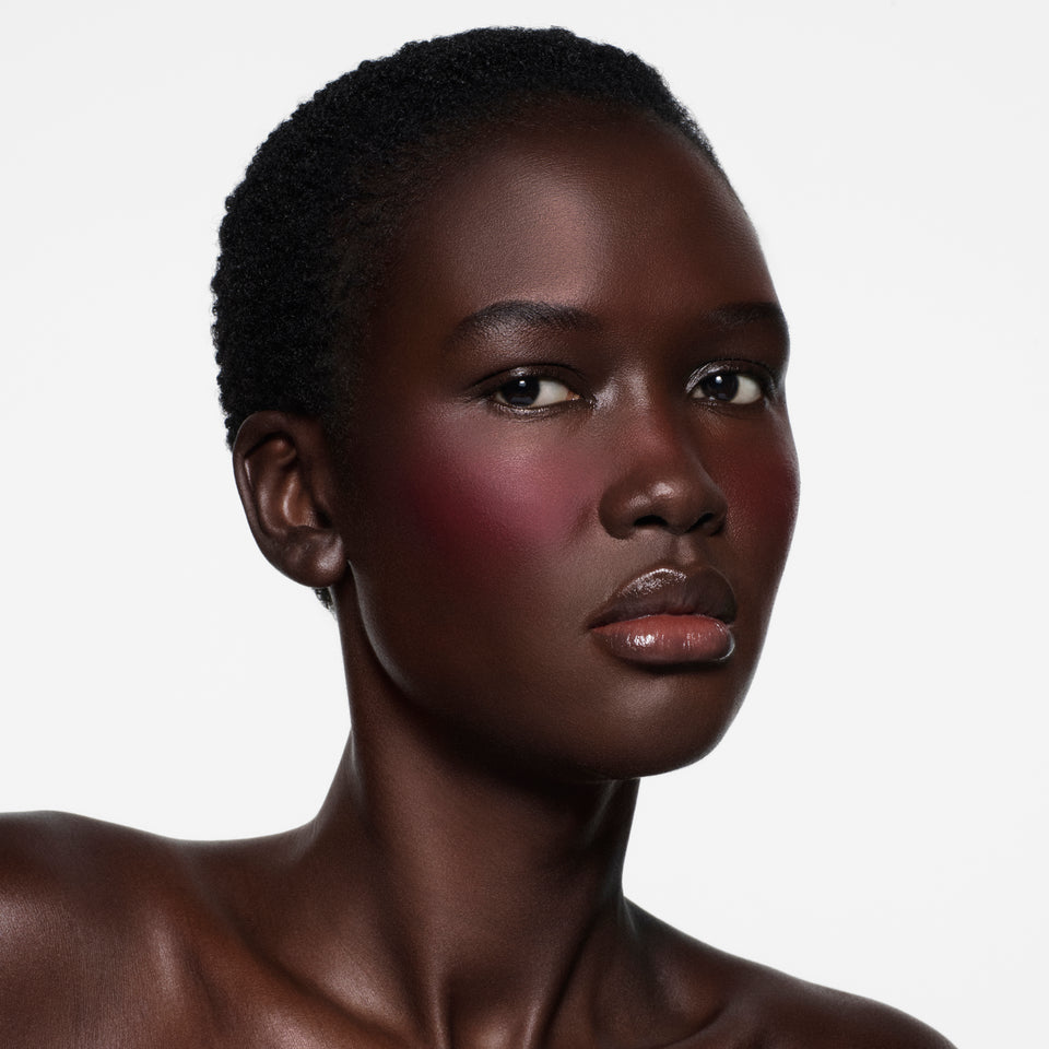 Deep-complexion model with cropped natural hair, raspberry flush on cheeks in Blush Stylus Fiore by Victoria Beckham Beauty.