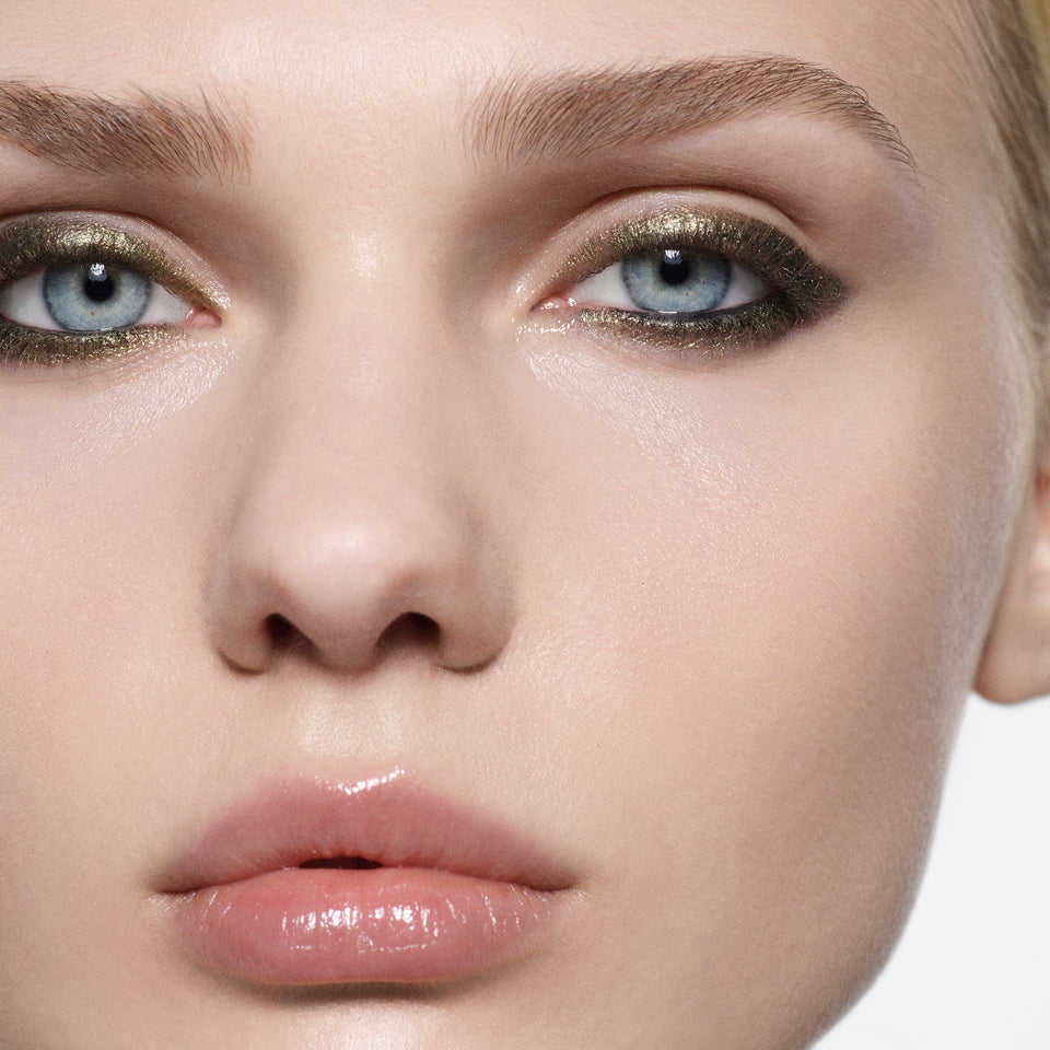 Close-up of a model's face showcasing metallic gold eyeshadow on her eyes and glossy pink lipstick on her lips.