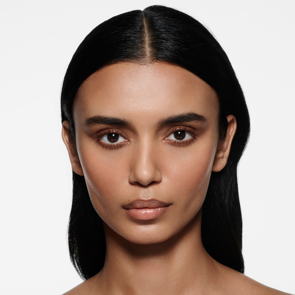 Tan-complexion model with sleek dark centre-parted hair wearing Posh Balm Soleil and Vast Lash Cocoa — Victoria Beckham Beauty.