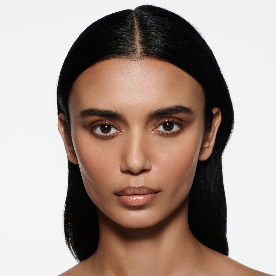 Tan-complexion model with sleek dark centre-parted hair wearing Posh Balm Soleil and Vast Lash Cocoa — Victoria Beckham Beauty.
