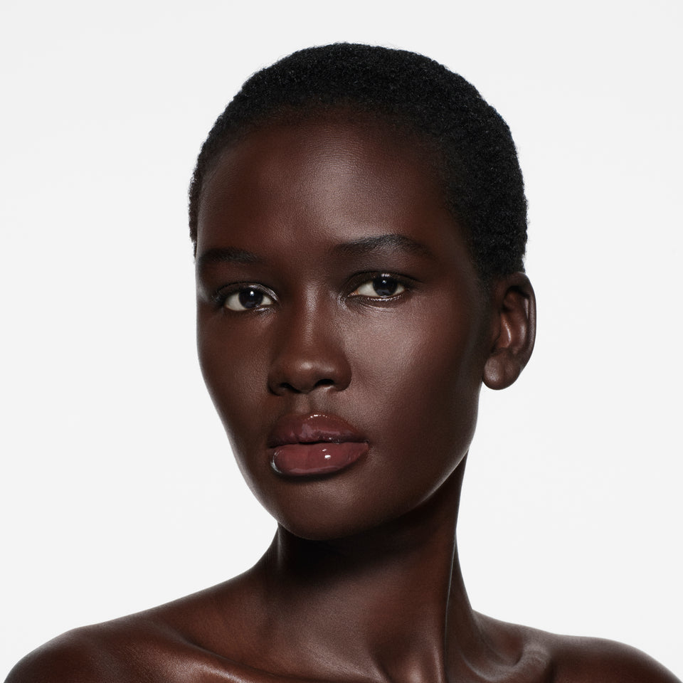 Deep-complexion model with short cropped natural hair, lips in Posh Gloss Aperitivo — rosewood-plum gloss by Victoria Beckham Beauty.