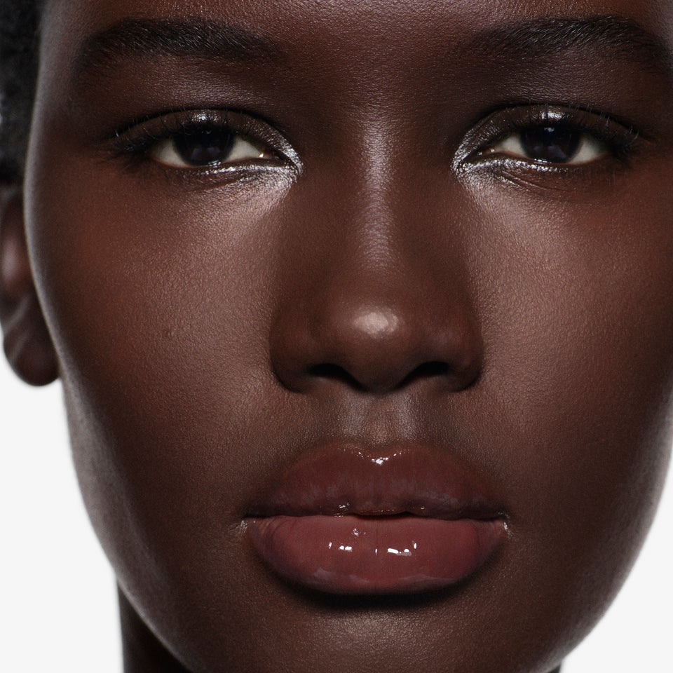 Close-up macro of glossy lips on deep complexion in Posh Gloss Aperitivo, Victoria Beckham Beauty's rosewood-plum lip gloss.