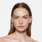 Fair-skinned model with sleek dirty-blonde hair in Posh Gloss Picante — vivid coral salmon by Victoria Beckham Beauty.