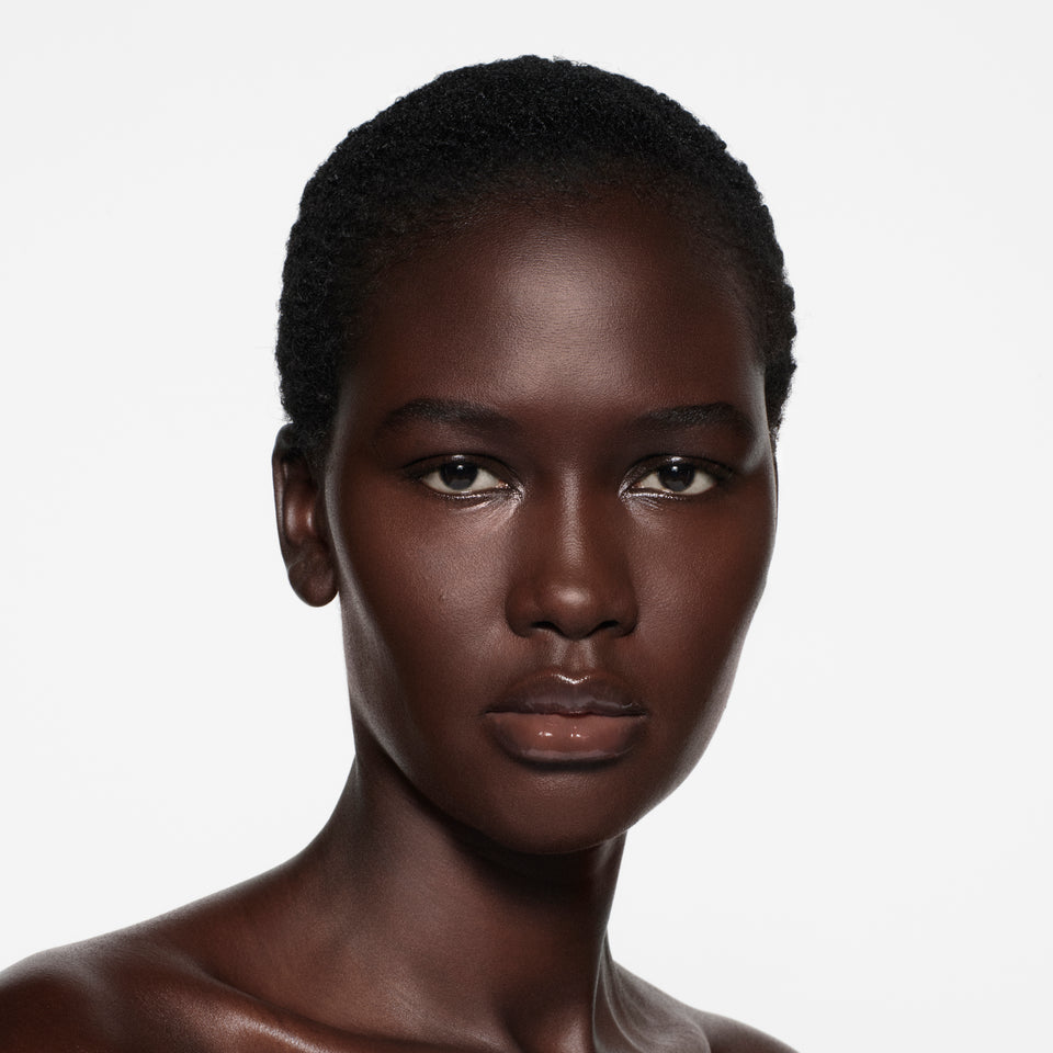 Deep-cocoa complexion with short cropped natural hair, lips in Posh Gloss Ice — clear high-shine gloss by Victoria Beckham Beauty.
