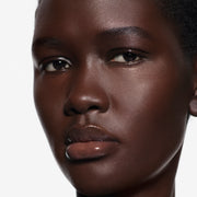 Close-up macro of lips on deep complexion glazed in Posh Gloss Ice — Victoria Beckham Beauty's clear mirror-finish lip gloss.