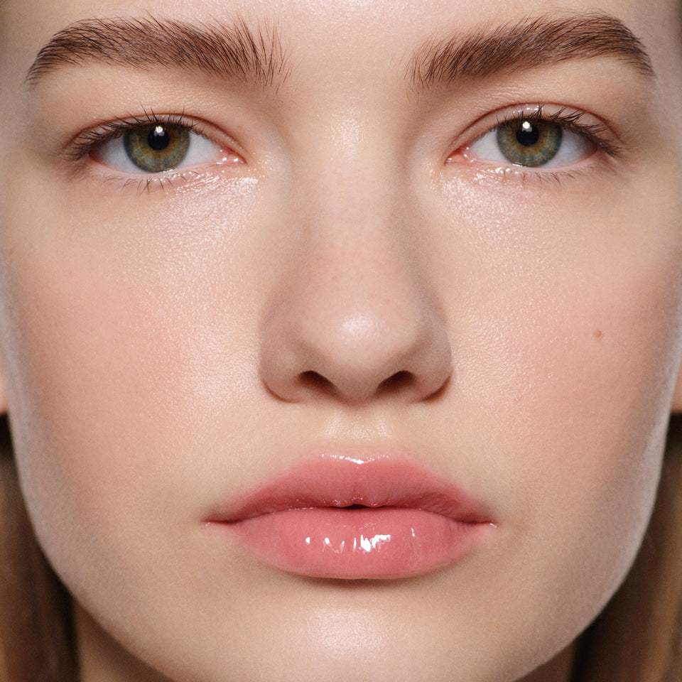 Macro of fair lips glossed in Posh Gloss Bungalow — Victoria Beckham Beauty's warm coral peach mirror-shine lip gloss.