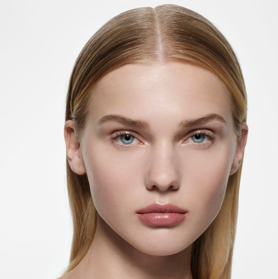Fair-skinned model with sleek centre-parted blonde hair wearing a soft rose nude Posh Lip — Victoria Beckham Beauty.
