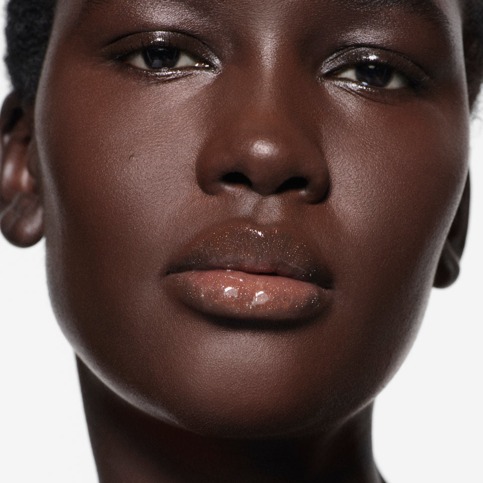 Close-up of lips on deep complexion in Posh Gloss Martini — Victoria Beckham Beauty's shimmering champagne gold lip gloss.