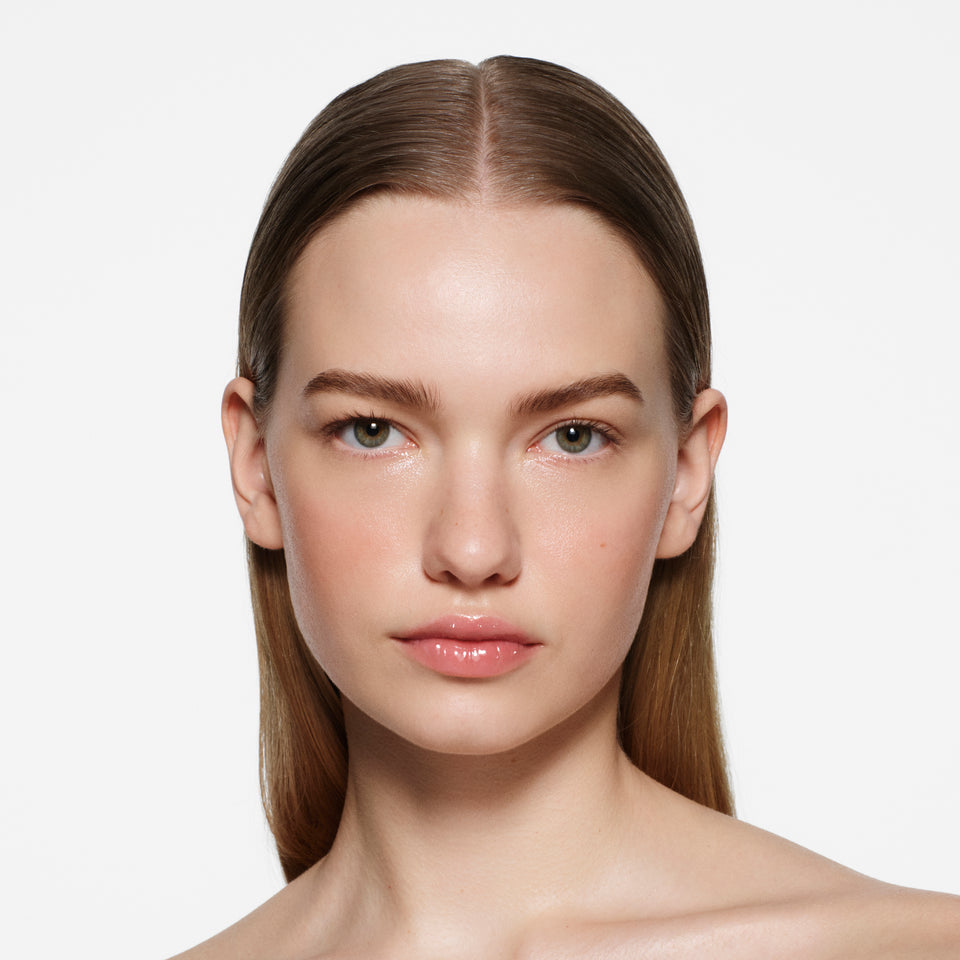 Fair-skinned model with slicked-back light brown hair in Posh Gloss Ice — Victoria Beckham Beauty's clear high-shine lip gloss.
