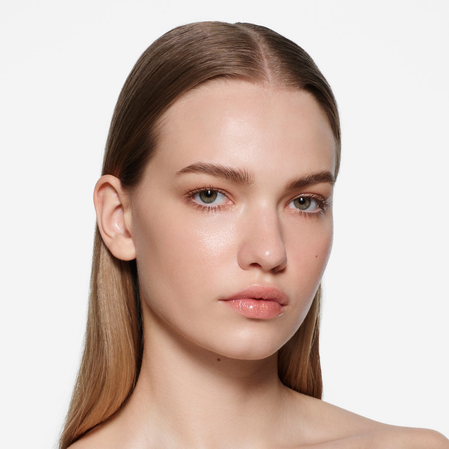 Fair-complexion model with long centre-parted hair wearing Posh Balm Soleil and Vast Lash Cocoa by Victoria Beckham Beauty.