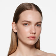 Fair-complexion model with long centre-parted hair wearing Posh Balm Soleil and Vast Lash Cocoa by Victoria Beckham Beauty.