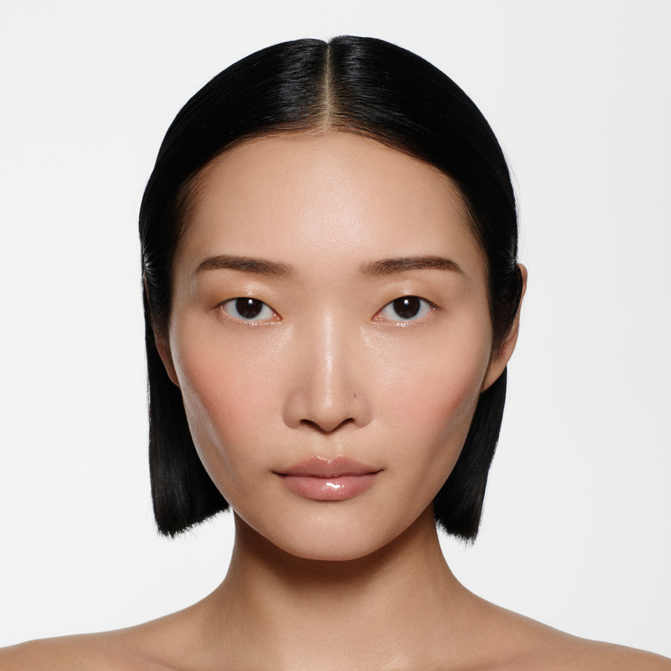 East Asian model with sleek dark bob wearing Posh Gloss Bikini, a milky peach nude lip gloss from Victoria Beckham Beauty.