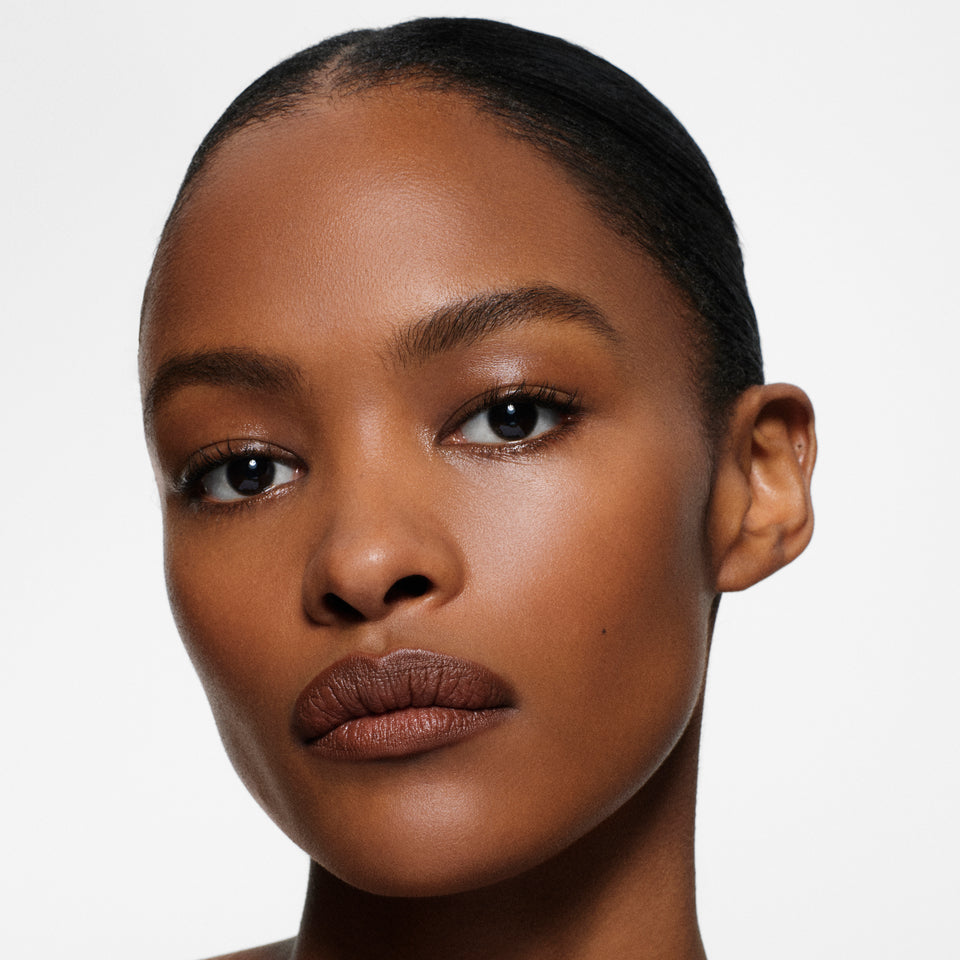 Deep-complexion model with sleek slicked-back hair in Lip Definer No. 05 — cocoa brown by Victoria Beckham Beauty.