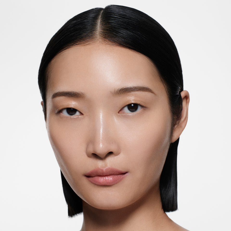 Warm-tan model with sleek centre-parted dark hair in Lip Definer No. 01 — dusty peach-rose by Victoria Beckham Beauty.