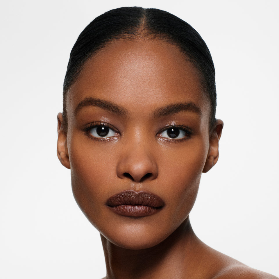 Deep-complexion model with sleek centre-parted dark hair in Lip Definer No. 06 — deep espresso by Victoria Beckham Beauty.