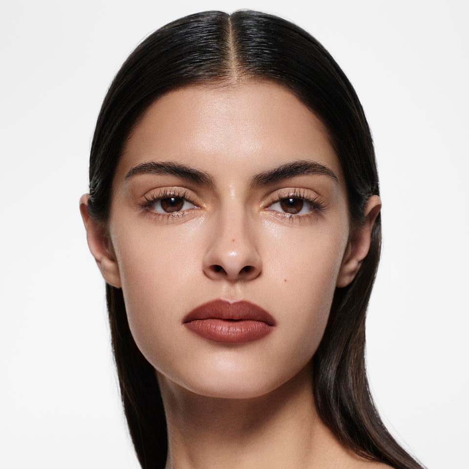 Olive-complexion model with sleek centre-parted dark hair in Lip Definer No. 04 — brick red-brown by Victoria Beckham Beauty.