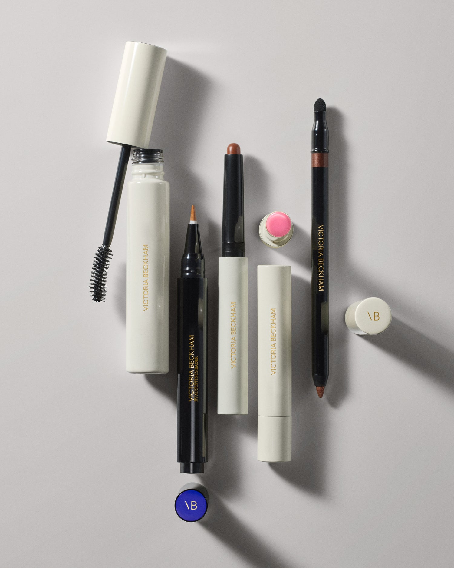 Set of makeup products including a mascara, lip liner, and other cosmetic tools on a light gray background.